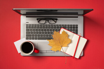 Top view photo of sticker note paper red cup of drink glasses pencil and autumn orange maple leaf on open red notebook on open grey laptop on isolated red background with blank space