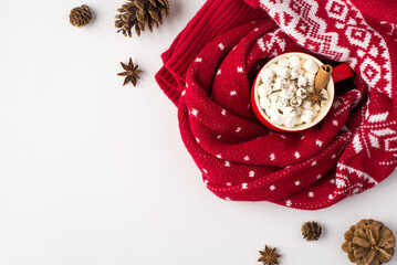 Top view photo of red cup of hot drinking with marshmallow and cinnamon stick wrapped in red sweater with ornament pine cones and anise on isolated white background with copyspace