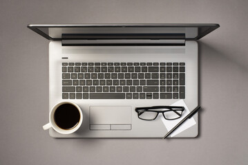 Top view photo of cup of coffee pen glasses and sticker note paper on grey laptop on isolated grey background