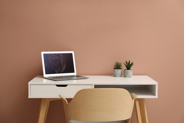 Stylish workplace with laptop and comfortable chair on beige background. Interior design