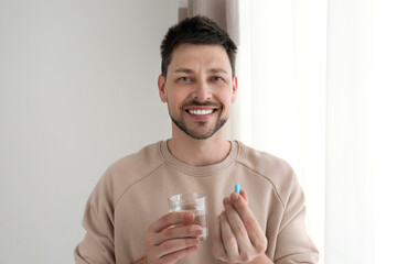 Man with glass of water taking pill at home - obrazy, fototapety, plakaty