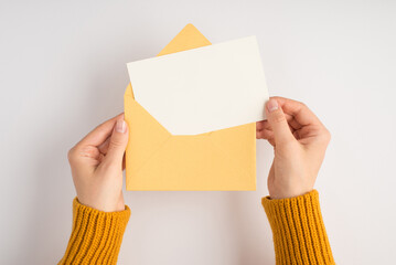 First person top view photo of female hands in yellow sweater holding open envelope with white card...