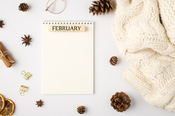 Top view photo of white sweater planner with inscription february pine cones dried lemon slices cinnamon sticks golden binder clips and stylish glasses on isolated white background with empty space