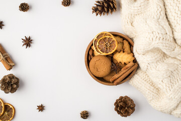 Top view photo of wooden bowl with cookies cinnamon sticks and dried lemon slices pine cones anise and white scarf on isolated white background with copyspace