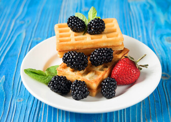 Sweet Homemade Berry Belgian Waffle on white plate over blue wooden background