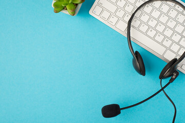 Top view photo of black headphones with microphone on white keyboard and flowerpot on isolated...
