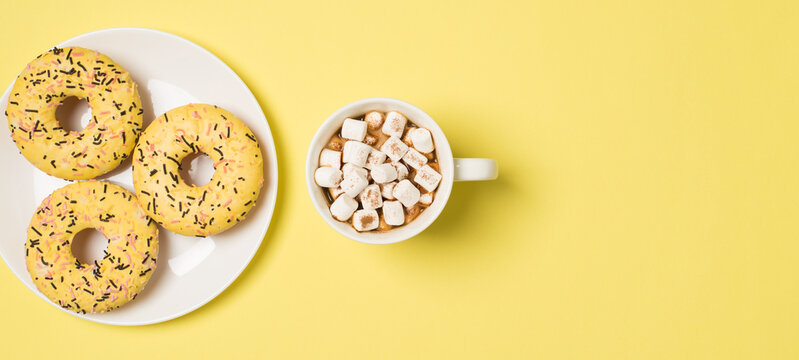 Top view photo of cup of drink with marshmallow and plate with three yellow glazed donuts on isolated pastel yellow background with copyspace