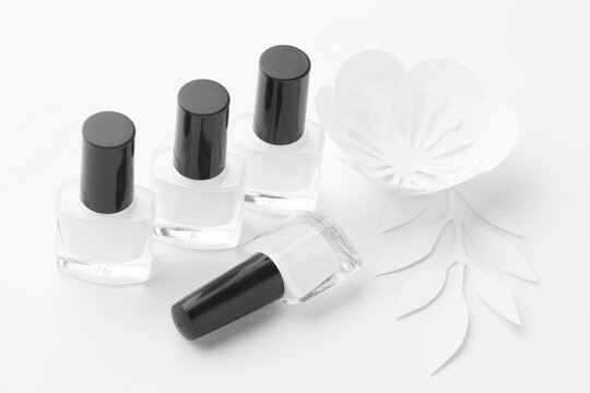 Bottles of white nail polish are aesthetically laid out on a white background with white paper flowers.