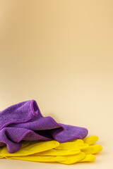 Purple microfiber cloth for washing and yellow rubber gloves on a neutral beige background, cleaning concept