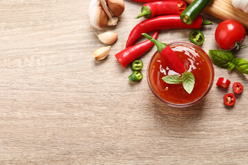 Spicy chili sauce and ingredients on wooden table, flat lay. Space for text