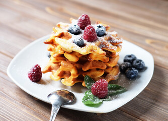 Traditional belgian waffles with fresh berrys and sugar powder on white plate, blue wooden background.