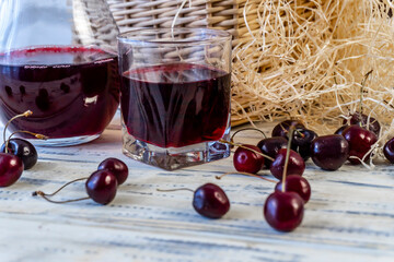 Cherry and cherry juice or wine on a wooden table, a decanter and a glass with juice, a basket with cherries