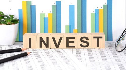 INVEST word written on the wood block with chart, glasses and pencils