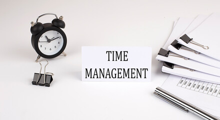 Card with text TIME MANAGEMENT on a white background, near office supplies and alarm clock. Business concept.