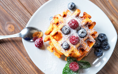 Homemade Belgian waffles served with fresh berries on white plate over wooden background, close up
