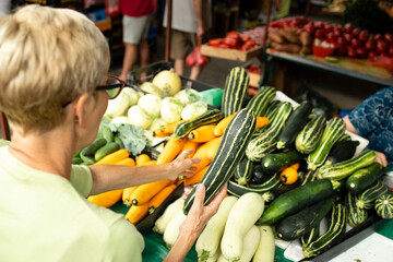Senior caucasian woman buying pumpkin at market place and holding bag full of healthy food.