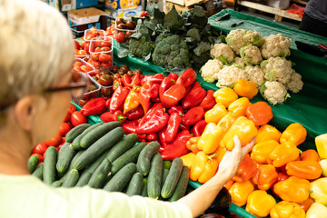 Top view of senior caucasian woman buying fresh organic vegetables and fruit at market place and holding bag full of healthy food.