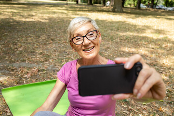 Senior caucasian woman using smart phone and taking selfie after workout.