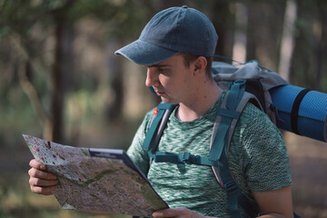 Young man consulting a map in the middle of a forest with a backpack and a mat on his back.