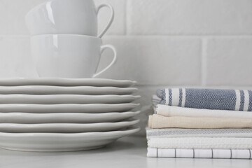 Fototapeta na wymiar Stack of soft kitchen towels and dishware on table near white brick wall, closeup