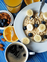 oatmeal with fresh berries on white plate with orange juice over blue wooden background.
