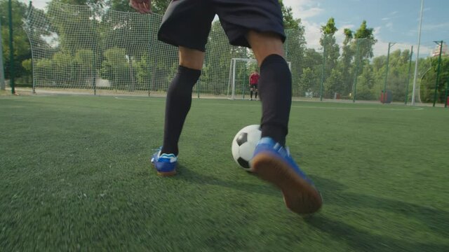 Close-up back view of soccer player legs in football boots and sportswear, dribbling to goal, demonstrating close ball control, quick feet, performing football tricks and moves, kicking ball on pitch