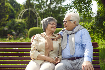 Happy loving senior couple sitting on bench and hugging looking into eyes. Aged retired family spouses feeling love showing adoration of each other enjoy rest and time together. Retirement concept