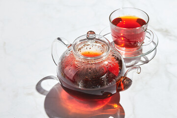Fruit tea with apples and thyme and honey in glass teapot and cup on white background with hard shadows