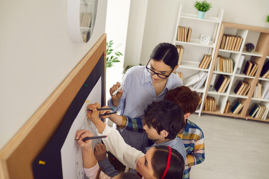 Female teacher deals with children in a modern creative school. Young junior students and their female teacher draw on a blackboard in the classroom. Concept of school life and the educational process - Powered by Adobe