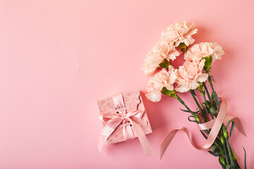 Bouquet of pink carnations and pink gift box. Design concept of holiday greeting with carnation bouquet on pink background