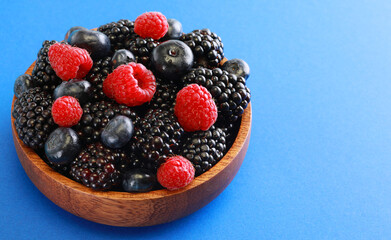 Fresh berries salad in a wooden plate on blue background.