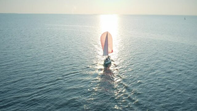 Aerial view of an unknown sailboat with pink sail moving on the sea in the evening