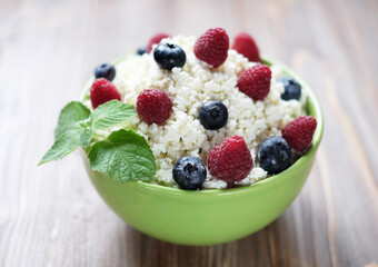 Cottage cheese in green bowl with raspberries and blueberries over wooden background.