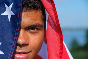 Close-up face of happy African-American man wraps himself in the U.S. flag and looks at the camera and smile outdoors in summer