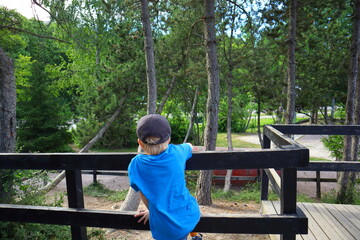 Kid with back towards camera at a playground. Blue shirt and cap. Little boy, summer time outside. Stockholm, Sweden, Europe.