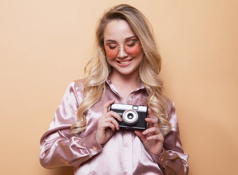 Portrait of a beautiful smiling young girl in pink shirt holding photo camera.