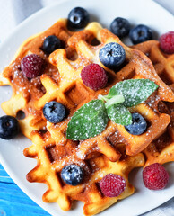 Homemade Belgian waffles served with fresh berries on white plate over wooden background, close up