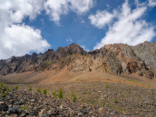 Atmospheric landscape with rocky mountain wall with pointy top in sunny light. Loose stone mountain slope in the foreground. Sharp stony mountains.