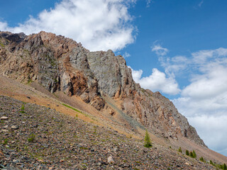 Atmospheric landscape with rocky mountain wall with pointy top in sunny light. Loose stone mountain slope in the foreground. Sharp stony mountains.