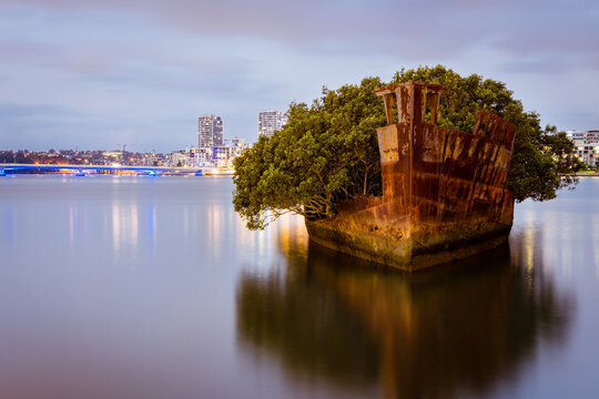 Shipwreck on river with cityscape long exposure