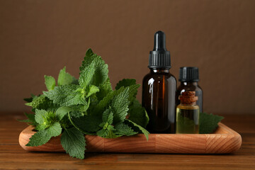 Tray with bottles of nettle oil and fresh leaves on wooden table against brown background