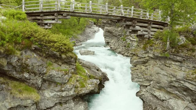 Flying Over A Rocky River Under Old Wooden Foot Bridge In Stryn, Norway. - Aerial Drone Forward Shot