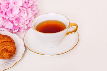 Cup of tea and croissants with hydrangea flower on white background