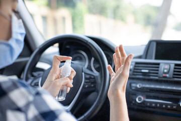 Young woman in face mask spraying hand sanitizer in the car