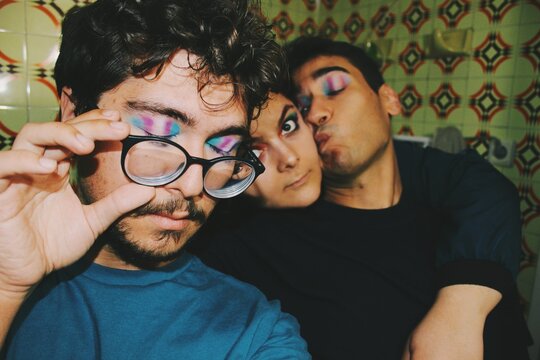 Closeup portrait of three queer friends faces wearing eyeshadow eye makeup of trans pride flag & lgbtq rainbow pride flag 