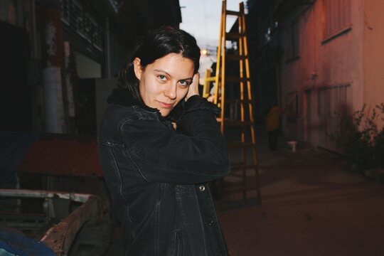 Portrait of young woman out at night in dark city street with flash light