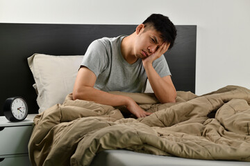 Depressed young Asian man sitting in bed cannot sleep from insomnia