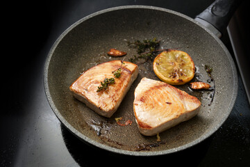 Tuna steaks n a frying pan with lemon, garlic and thyme on a back stove, copy space