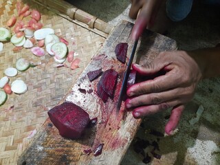 Cutting beet with sharp chef knife on cutting board. The beetroot is the taproot portion of a beet plant. Its other names table beet, garden beet, red beet, dinner beet or golden beet.