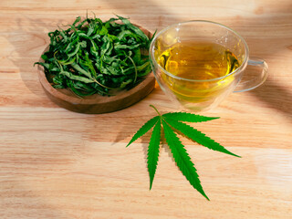 A glass of hot marijuana tea on the wooden table. Cannabis herbal tea with dried leaves
